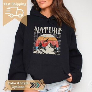 Può includere: Felpa con cappuccio nera con una grafica in stile vintage di una catena montuosa e un tramonto. La grafica presenta la parola "NATURE" ripetuta più volte.