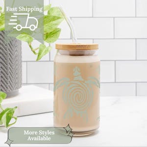 May include: A clear glass tumbler with a bamboo lid and a sea turtle design. The tumbler contains a light brown beverage and a clear straw. The words "Fast Shipping" and "More Styles Available" are also visible.