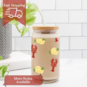 May include: A clear glass tumbler with a bamboo lid and a glass straw. The tumbler is decorated with red lobster and yellow lemon graphics. The words "Fast Shipping" and "More Styles Available" are displayed on the image.