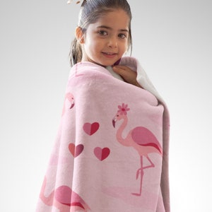 Flamingos in Love Throw Blanket Adult Minky Blanket with a child model wrapped in a pink blanket with flamingos and hearts printed all over and name personalization area.