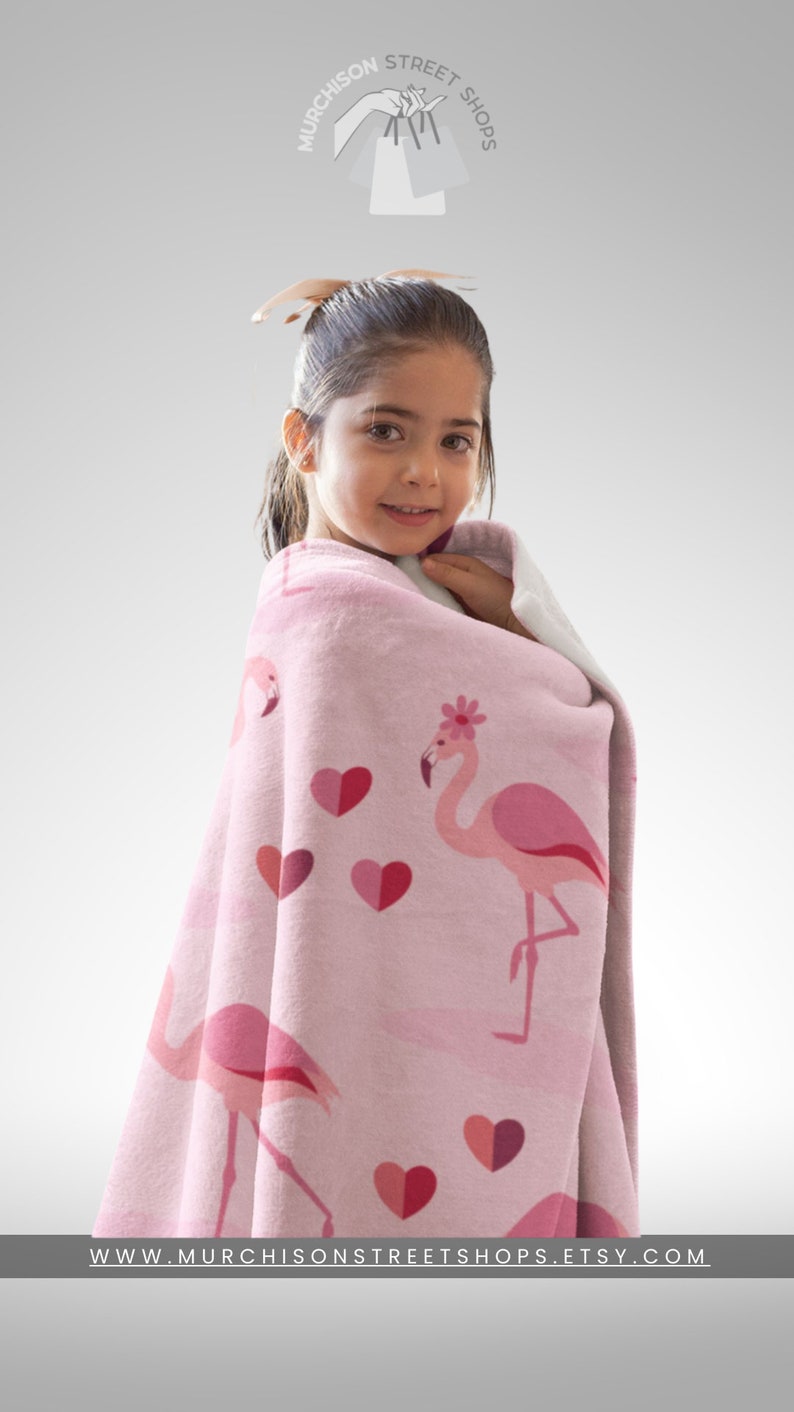 Flamingos in Love Throw Blanket Adult Minky Blanket with a child model wrapped in a pink blanket with flamingos and hearts printed all over and name personalization area.