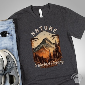 Forest Themed T Shirt Pine Tree Nature Shirt with a flat layout of a dark gray tshirt showing a mountain scene and the words Nature is the best therapy