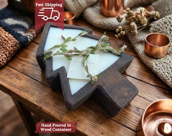 May include: A tree-shaped candle in a dark wood container. The white candle is decorated with greenery and a tag that reads "Cozy Cabin". The candle sits on a wooden table with other copper items.
