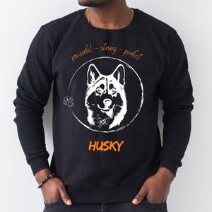 Könnte beinhalten: Schwarzes Sweatshirt mit einer weißen Illustration eines Husky-Hundes in einem Kreis. Das Wort "HUSKY" ist orangefarben unter dem Bild gedruckt. Über dem Bild stehen die Worte "powerful - strong - perfect" in Orange.