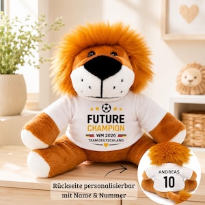 Könnte beinhalten: Ein Stofftier-Löwe mit einem weißen T-Shirt mit der Aufschrift "FUTURE CHAMPION WM 2026 TEAM DEUTSCHLAND". Der Löwe hat einen braunen Körper, eine orangefarbene Mähne und eine schwarze Nase. Der Text "Rückseite personalisierbar mit Name & Nummer" ist ebenfalls sichtbar.