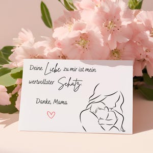May include: A white card with the text "Deine Liebe zu mir ist mein wertvollster Schatz. Danke, Mama" and a line drawing of a mother and child. A small red heart is drawn below the text. Pink flowers are in the background.