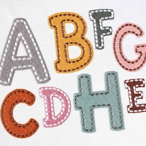 Może przedstawiać: Wyhaftowane filcowe litery w różnych kolorach, w tym szary, żółty, różowy, brązowy i zielony, tworzące słowo "ABCDEFGH"