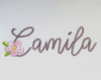 May include: Embroidered name "Camila" in cursive script with a pink flower and green leaves.
