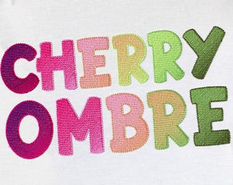May include: Embroidered "CHERRY OMBRE" text in a rainbow of colors, with each letter having a gradient effect. The letters are stitched in a bold, blocky font.