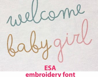 May include: Embroidery font design for "welcome baby girl" in teal, gold, and pink thread. The text is stitched on a white fabric background. The text "ESA embroidery font" is below the design, along with the text "Hatch, Wilcom E series, or Janome V5 embroidery software".