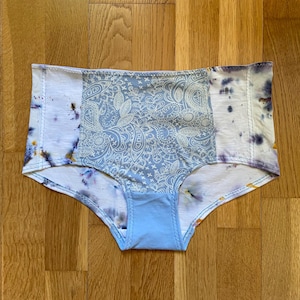 Könnte beinhalten: Blaue und weiße gemusterte Unterwäsche mit Batik-Design. Die Unterwäsche hat ein weißes Paisley-Muster auf hellblauem Hintergrund. Die Seiten sind in Weiß mit blauen und gelben Akzenten gefärbt.