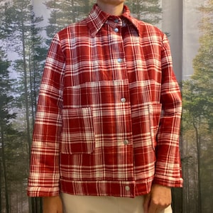 May include: A red and white plaid jacket with a collared neckline and two front pockets. The jacket has silver snap closures and is made of a quilted fabric. The pattern is a classic plaid design.