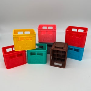 Könnte beinhalten: Eine Sammlung farbenfroher Miniatur-Batteriekisten in Rot, Gelb, Türkis, Rosa, Braun, Blau und Grau. Jede Kiste hat eine rechteckige Form mit einem gitterartigen Innenraum und dem Text "AA Batterie" oder "CR123 Batterie".