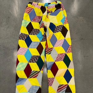 May include: Colorful patchwork pants with a geometric design. The pants feature a variety of fabric patterns and colors, including yellow, blue, red, and brown. The pants have a relaxed fit and a light blue trim at the bottom.