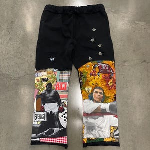 May include: Black sweatpants with a patchwork design featuring images of boxers, including Muhammad Ali and a bee motif. The sweatpants have a drawstring waist.