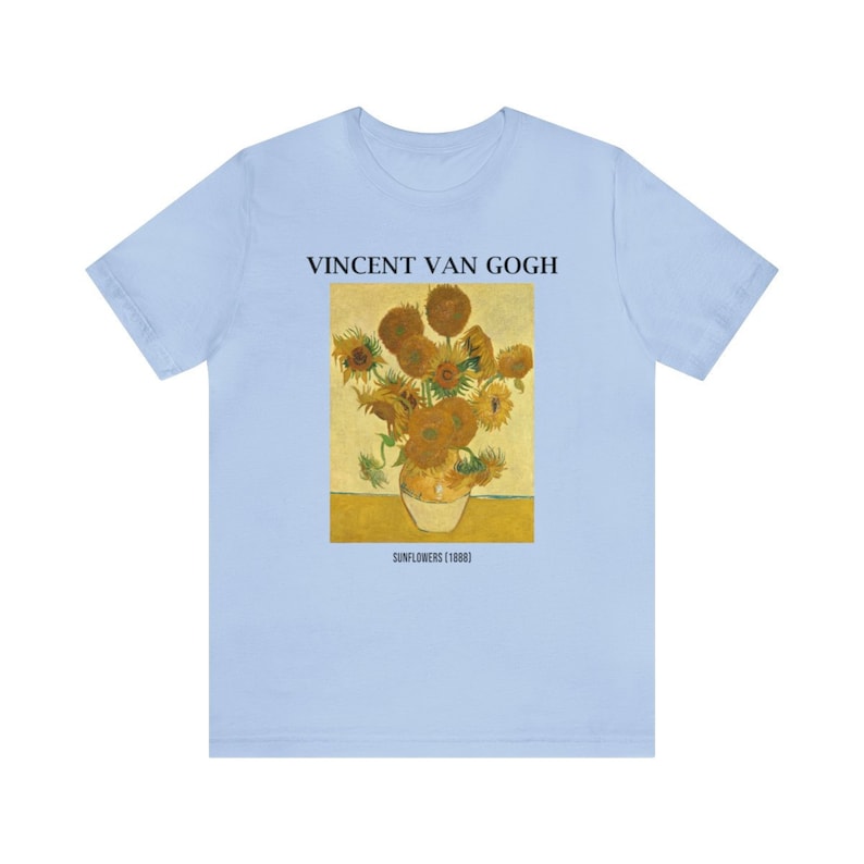 May include: Pale blue t-shirt displaying Vincent Van Gogh's "Sunflowers (1888)" painting. The image shows a vase of sunflowers in yellow and brown hues. The text "VINCENT VAN GOGH" and "SUNFLOWERS (1888)" are printed above and below the artwork.