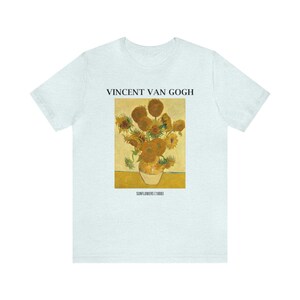May include: Pale blue t-shirt with a print of Vincent Van Gogh's "Sunflowers" painting. The artwork depicts a vase of sunflowers in yellow and brown hues. The text "VINCENT VAN GOGH" and "SUNFLOWERS (1888)" are printed above and below the artwork.