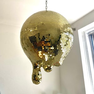 May include: A gold disco ball with a dripping effect, hanging from a silver chain.