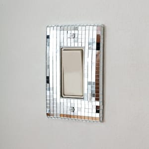 May include: A white light switch with a decorative silver mosaic tile cover.