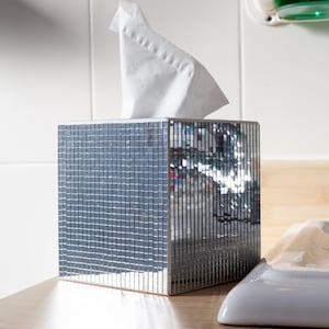 Peut inclure: Un porte-mouchoirs en miroir argenté avec un mouchoir en papier blanc à l'intérieur. Le porte-mouchoirs est fait de petites tuiles carrées.
