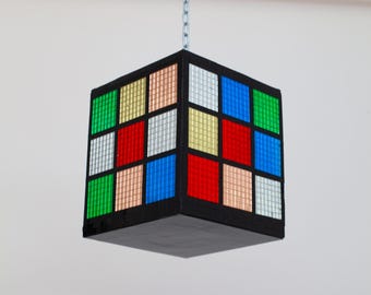 May include: A black cube-shaped hanging light fixture with a chain. The cube is made up of 16 smaller squares, each with a different color: green, gold, pink, white, blue, and red.