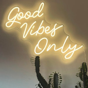 May include: White neon sign with the text "Good Vibes Only" on a white wall. The sign is hanging from the ceiling and is illuminated.
