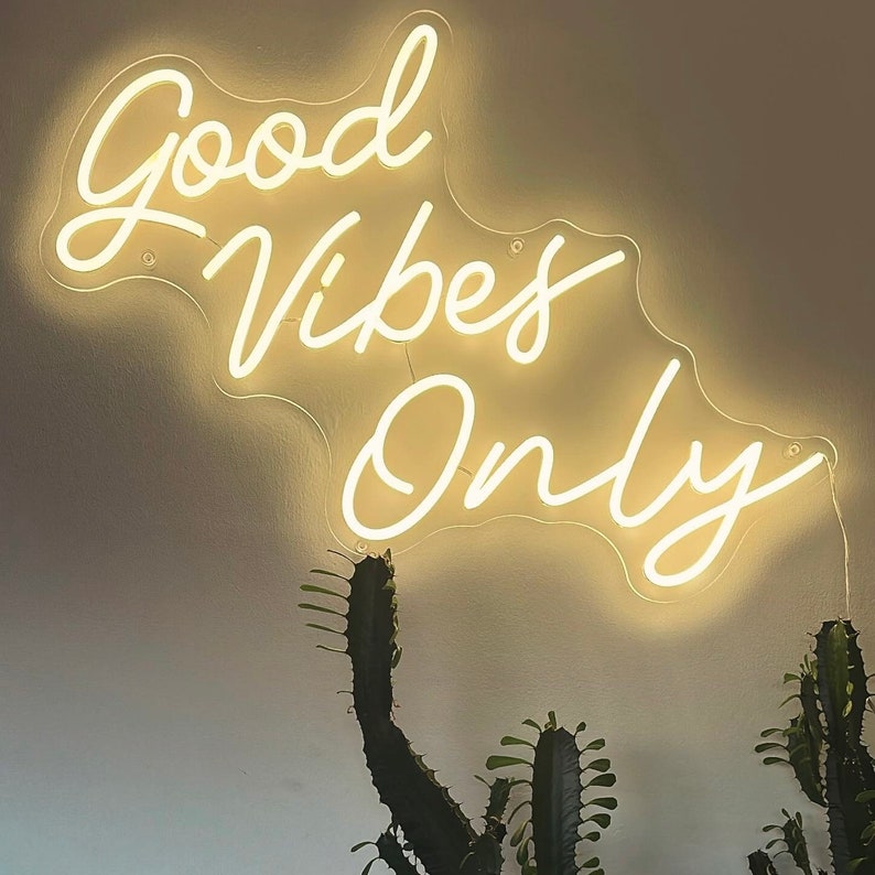 May include: White neon sign with the text "Good Vibes Only" on a white wall. The sign is hanging from the ceiling and is illuminated.