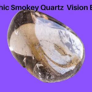 Puede incluir: Un cristal de cuarzo ahumado, un tipo de cuarzo de color marrón oscuro a negro, con una superficie lisa y redondeada. El cristal es translúcido y tiene un ligero brillo. El cristal está colocado sobre un fondo morado.