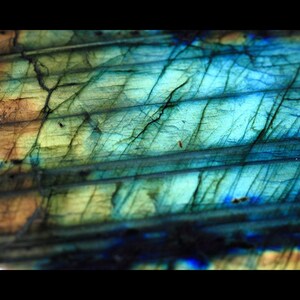 May include: Close-up of a labradorite gemstone with iridescent blue, green, and gold hues. The stone has a striated pattern and a smooth, polished surface.