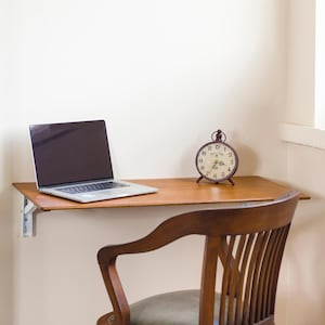 Peut inclure: Un bureau mural en bois avec un ordinateur portable et une horloge vintage sur le dessus. Une chaise en bois avec un siège en cuir marron se trouve devant le bureau.