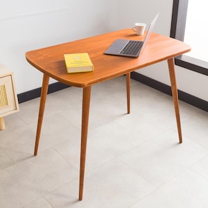 May include: A light brown wooden table with a rounded top and four slender legs. A laptop computer and a book are on the table.