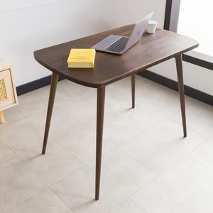 May include: A dark brown wooden table with a rectangular top and four slender legs. A laptop computer and a book are on the table.