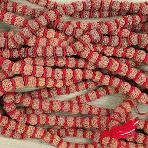 May include: A close-up of a long strand of brown beads with red string wrapped around them. The beads are arranged in a circular pattern and are tied together with a red tassel.