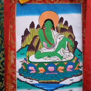 May include: A green deity figure sits in a meditative pose on a lotus flower. The figure is surrounded by mountains and a body of water. The deity has a halo and is wearing a white robe.
