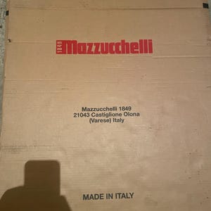 Peut inclure: Une boîte en carton marron clair avec le logo Mazzucchelli en rouge. Le texte sur la boîte indique "Mazzucchelli 1849" et "Made in Italy". On y trouve une adresse italienne.