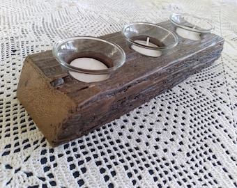 May include: A rustic wooden candle holder with three glass candle cups. The holder is made of reclaimed wood and has a natural, weathered finish.