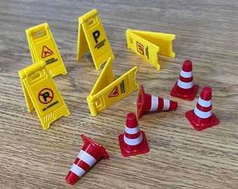 May include: A collection of miniature construction signs and traffic cones. The signs are yellow with black symbols and text, including a warning symbol and the words "No Parking". The cones are red with white stripes.