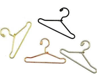 Könnte beinhalten: Vier Drahtkleiderbügel in Gold, Schwarz, Kupfer und Silber. Die Kleiderbügel sind auf weißem Hintergrund angeordnet. Jeder hat einen Haken und einen dreieckigen Körper, zum Präsentieren von Kleidung.