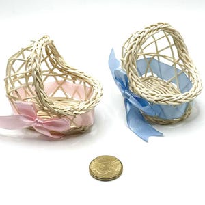 May include: Two small, woven wicker baskets with heart-shaped designs. One basket has a pink ribbon, the other a blue ribbon. A gold coin is next to the baskets. The baskets are likely for decorative purposes or small gifts.