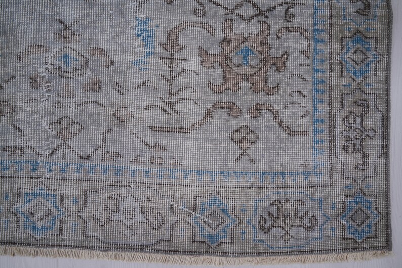 May include: Close-up of a light gray rug with a blue and brown floral pattern. The rug has a fringe border.
