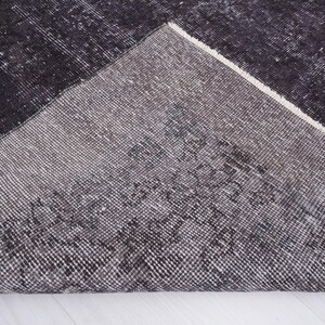 Puede incluir: Una secci&oacute;n de una alfombra gris oscuro y negra con una apariencia desgastada y vintage. La alfombra tiene un patr&oacute;n geom&eacute;trico y un borde blanco. La textura es visible, lo que sugiere un material tejido. La alfombra est&aacute; parcialmente enrollada, revelando la parte inferior.