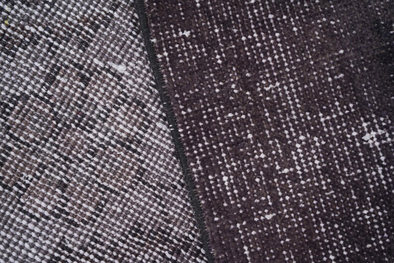 Puede incluir: Primer plano de una secci&oacute;n de una alfombra estampada en gris oscuro y blanco. La alfombra tiene un aspecto texturizado con un patr&oacute;n repetitivo de peque&ntilde;as formas irregulares. La paleta de colores es principalmente gris oscuro y blanco.