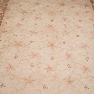 May include: A beige area rug with a floral pattern. The rug has a brown border with a vine and leaf design.