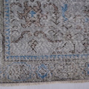 May include: A vintage rug with a light gray background and a floral pattern in shades of brown and blue. The rug has a fringed edge.
