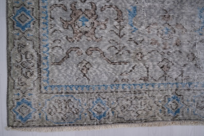 May include: A vintage rug with a light gray background and a floral pattern in shades of brown and blue. The rug has a fringed edge.