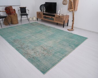 May include: A teal blue vintage rug with a faded floral pattern. The rug is laid out on a light wood floor in a living room setting.