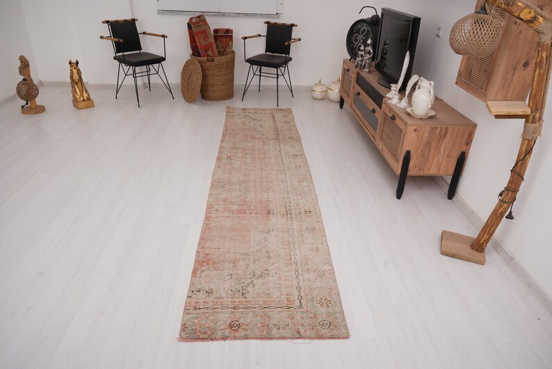 May include: A light pink and cream colored vintage runner rug with a floral pattern. The rug is laid out on a white wood floor in a room with furniture.