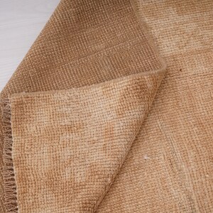 May include: A close-up of a folded brown rug with a textured weave. The rug has a subtle ombre effect, with a lighter shade of brown at the edges.