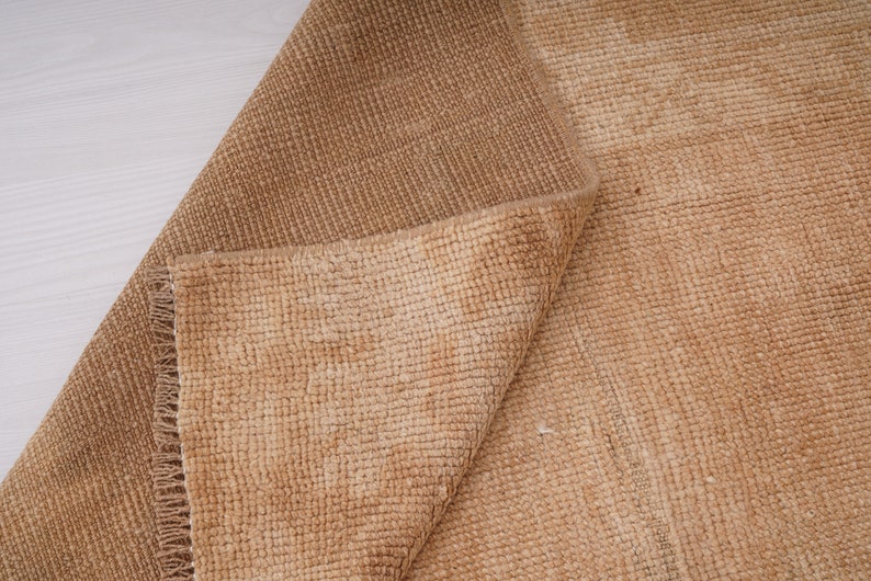 May include: A close-up of a folded brown rug with a textured weave. The rug has a subtle ombre effect, with a lighter shade of brown at the edges.