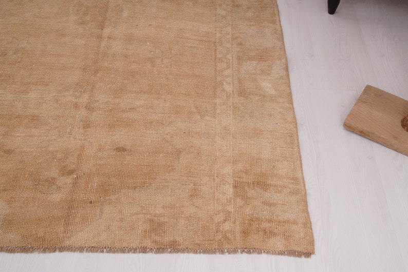 May include: A light brown rug with a subtle pattern. The rug has a fringed edge and is made of a soft, woven material.